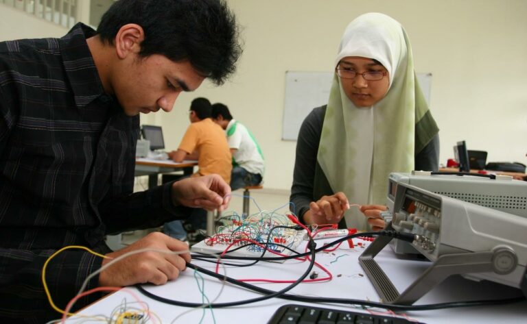 two-students-look-at-a-board-with-electric-wires